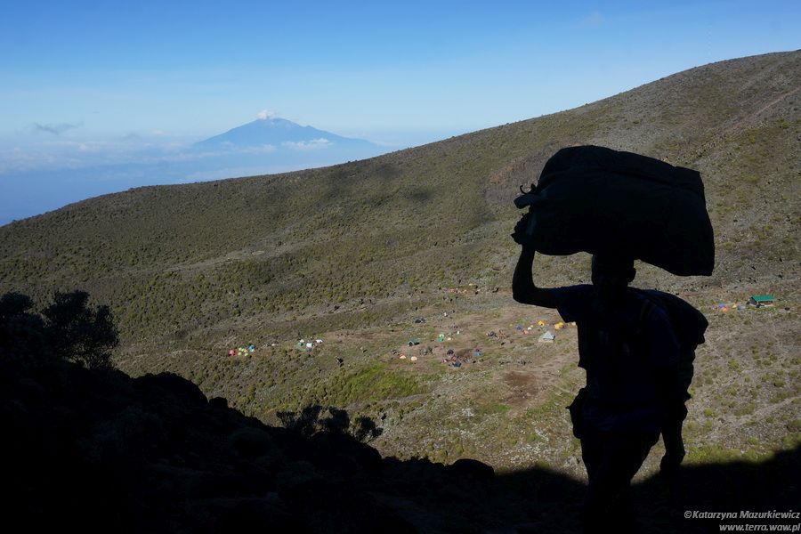 Tragarz wchodzący na Kilimandżaro, w tle wulkan Meru
